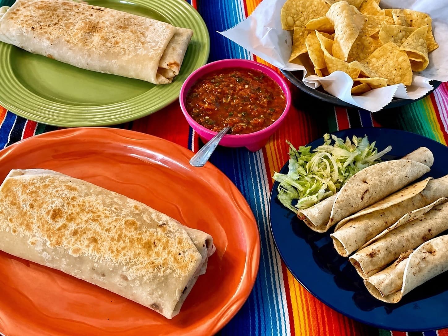 Burritos, rolled tacos, chips, and salsa on colorful serape tablecloth