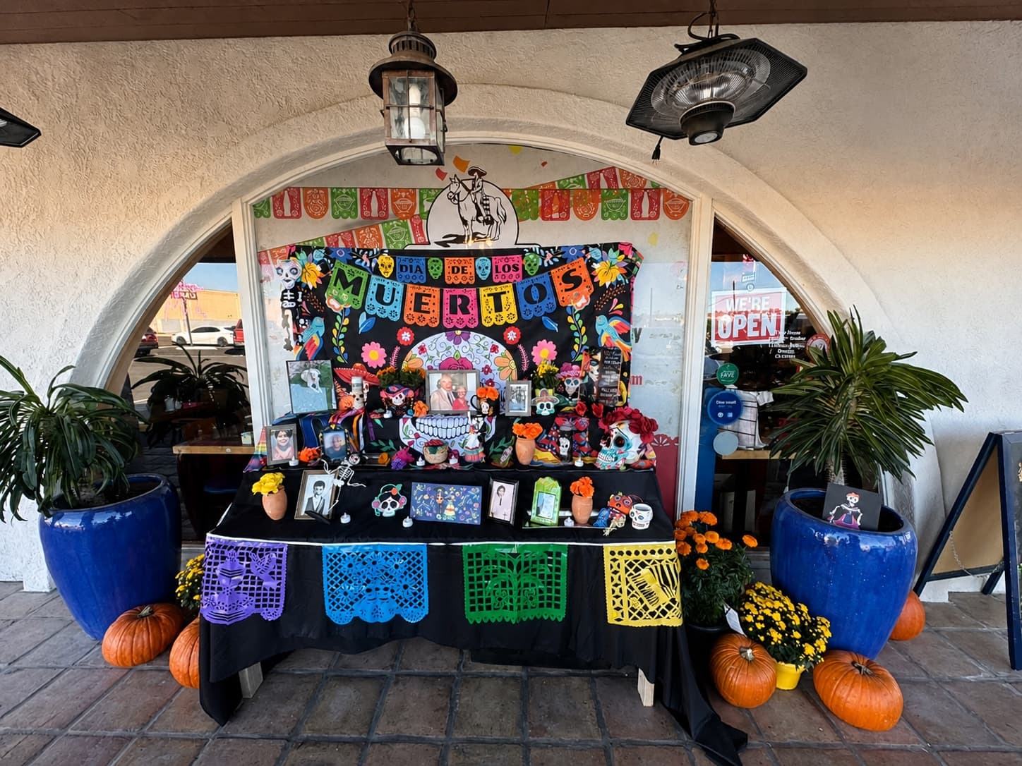 Dia de los Muertos display outside El Charro with flowers, pumpkins, and family photos