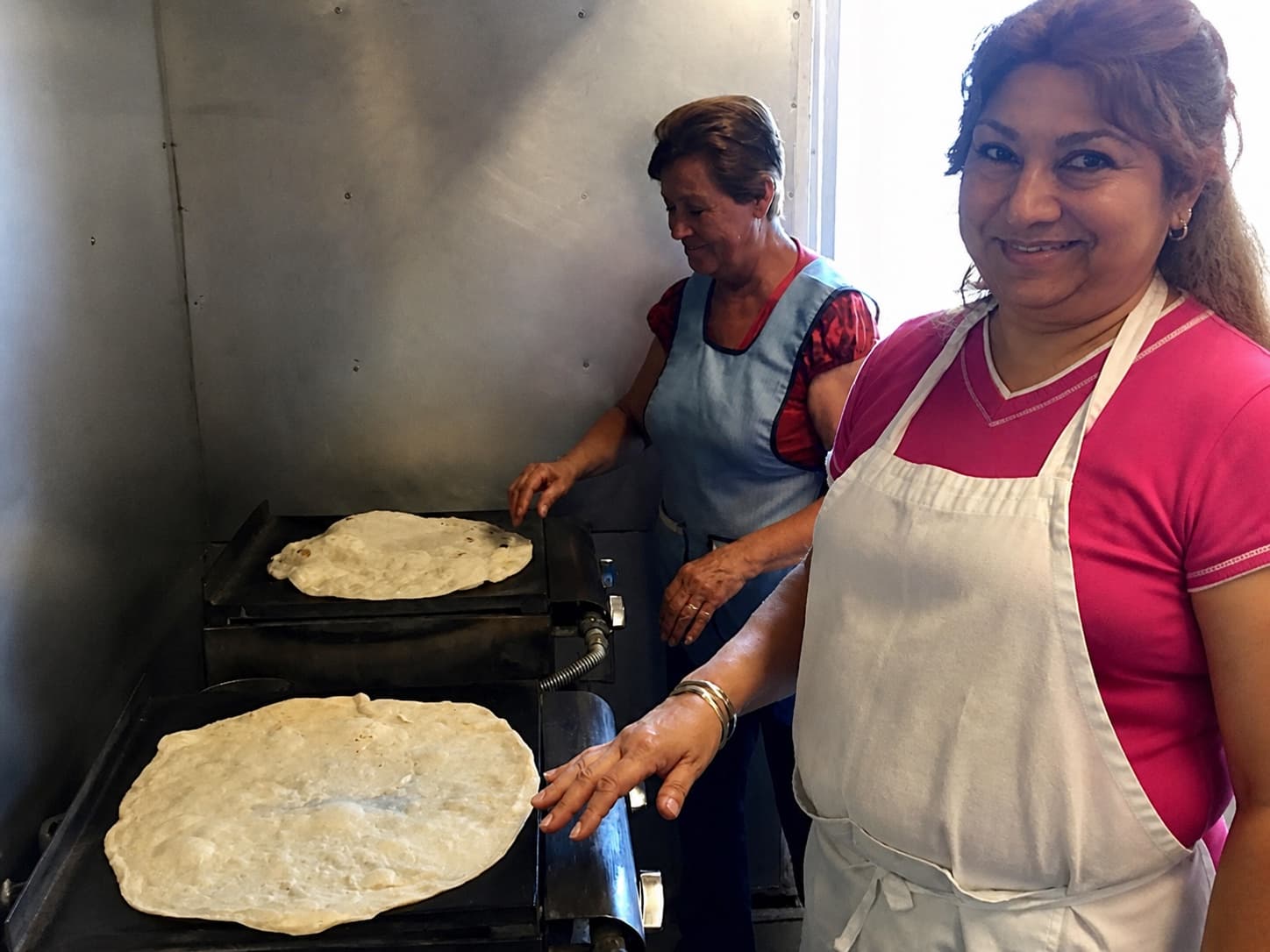 Two team members making homemade flour tortillas on the griddle