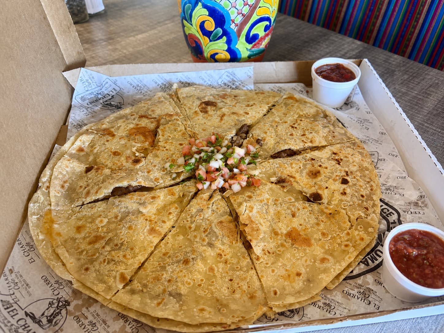 Large quesadilla cut into slices in a takeout box with salsa