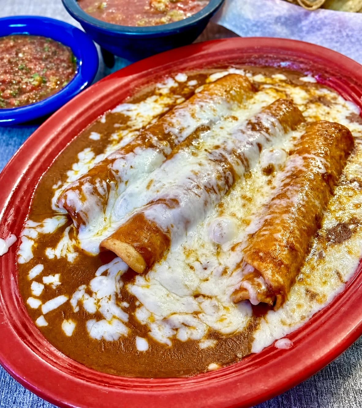 Red enchiladas covered with melted cheese and sauce on a red plate
