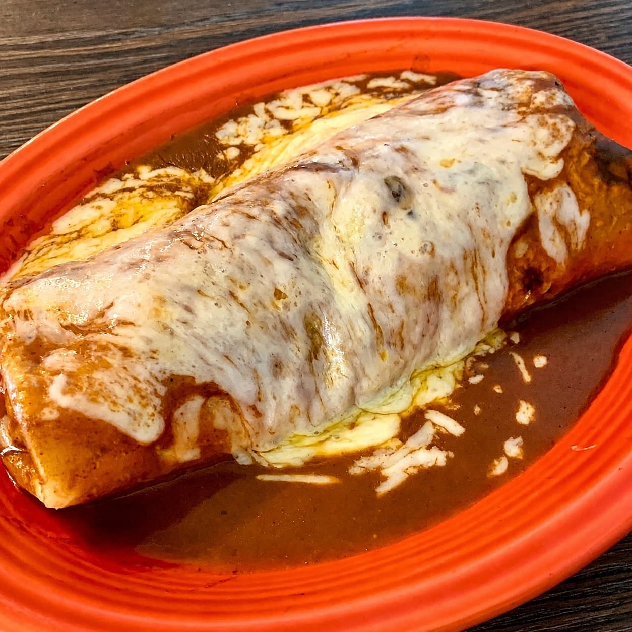 Red Saddle burrito covered in sauce and melted cheese on an orange plate