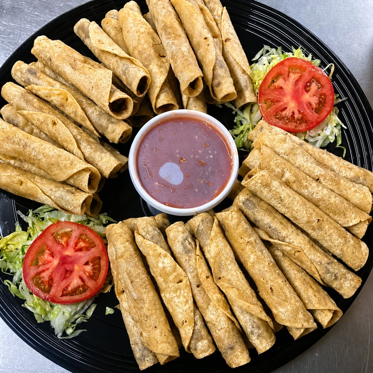 Rolled taco catering platter with tomato, lettuce, and sauce