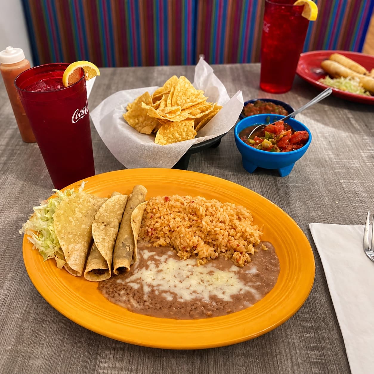 Rolled taco dinner with rice, beans, chips, salsa, and drinks