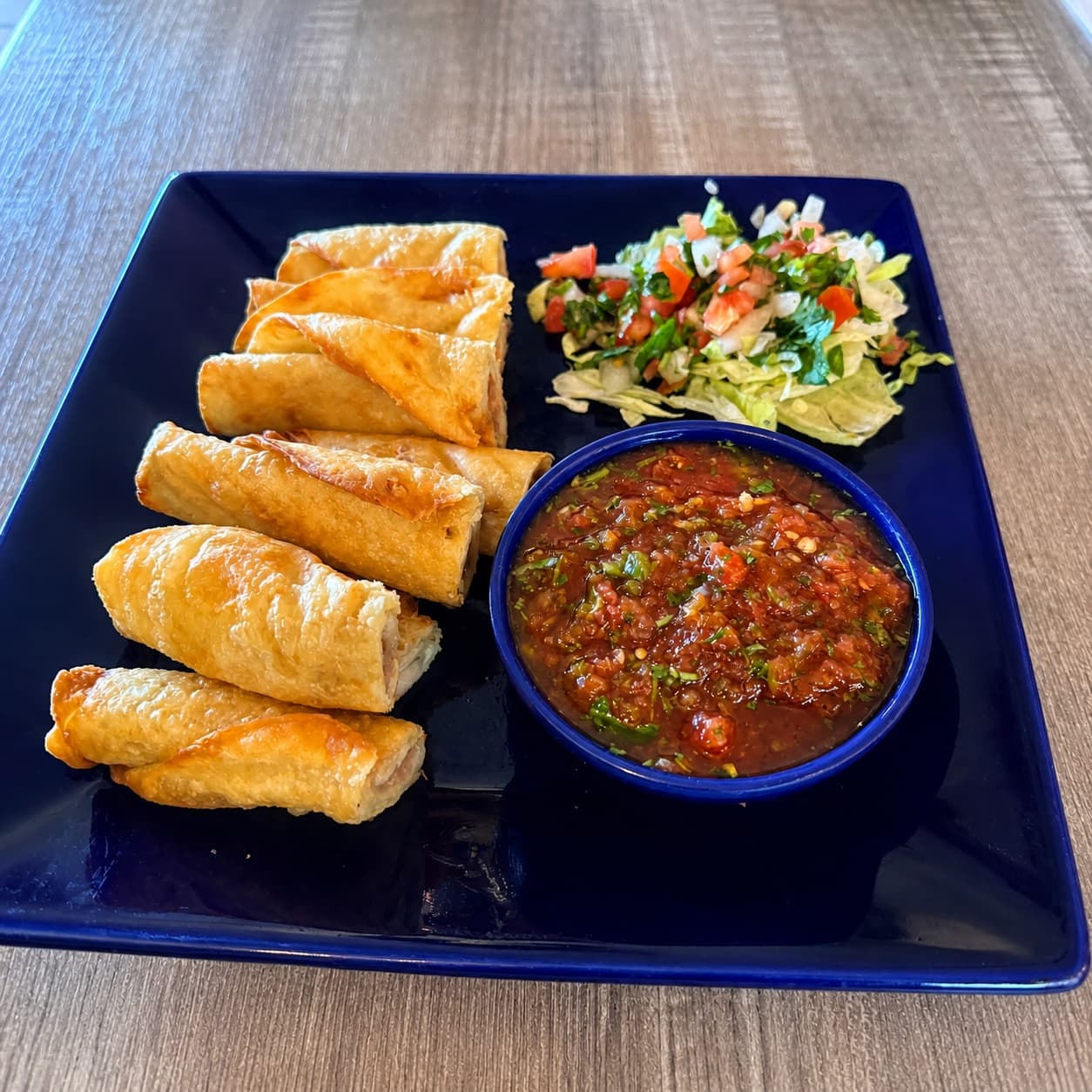Rolled tacos with salsa and lettuce on a blue plate
