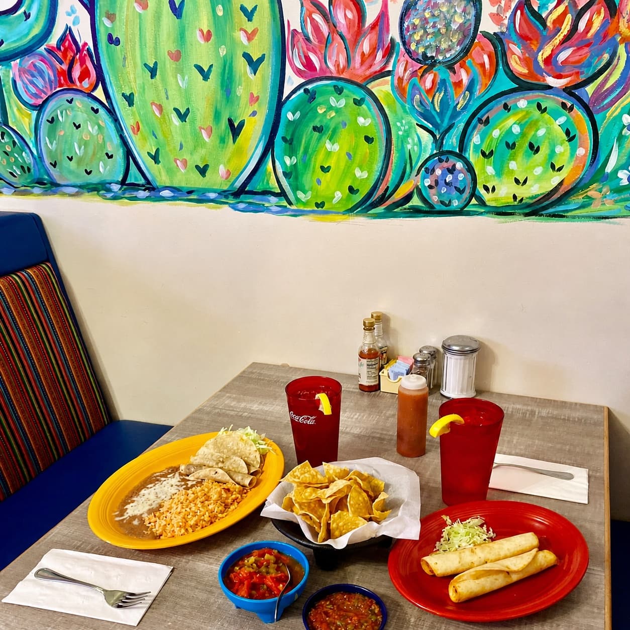 El Charro table with plates and drinks beneath a colorful cactus mural